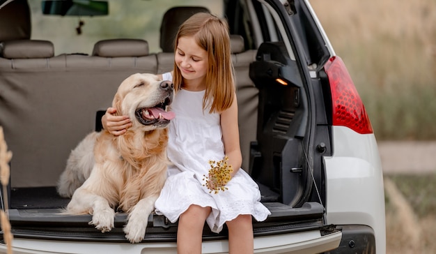 Preteen dziewczyna z golden retriever pies siedzi w bagażniku samochodu razem. ładne dziecko przytula pieska w pojeździe