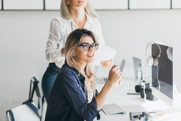 Pretty freelancer dziewczyna siedzi w pobliżu komputera z czarnym ekranem i odwraca wzrok z uśmiechem