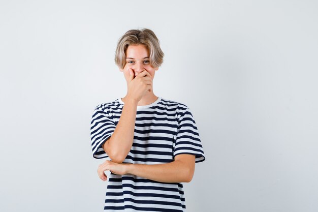 Pretty teen boy w paski t-shirt z ręką na ustach i patrząc szczęśliwy, widok z przodu.