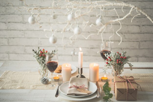 Prezent, talerze, sztućce, świece i dekoracje ułożone na stole na świąteczny obiad