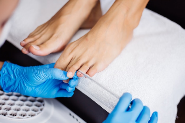 Proces pedicure Pedicure w salonie domowym Pielęgnacja stóp i paznokci Proces profesjonalnego pedicure Mistrz w niebieskich rękawiczkach wykonuje pedicure