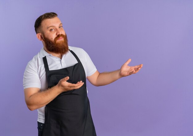 Profesjonalny brodaty fryzjer w fartuchu, prezentując z bronią kopia przestrzeń uśmiechnięty pewnie stojący nad fioletową ścianą