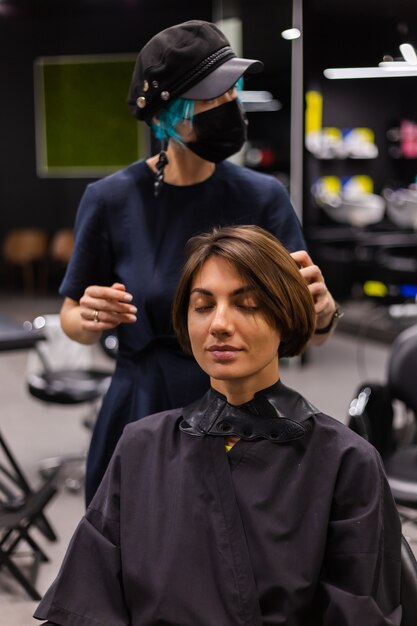 Profesjonalny fryzjer dziewczyna wykonuje fryzurę klienta. Dziewczyna siedzi w masce w salonie piękności