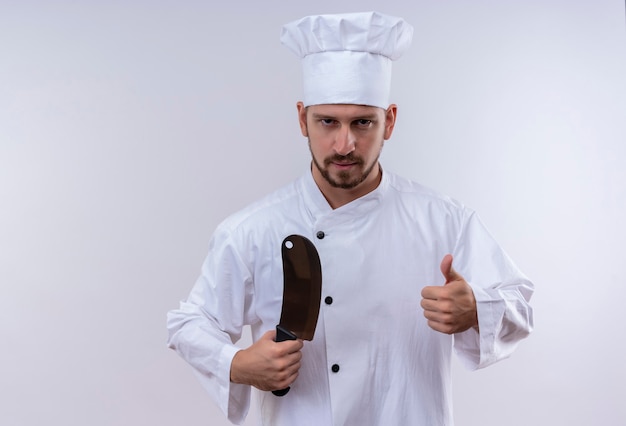 Profesjonalny kucharz mężczyzna w białym mundurze i kapelusz kucharz trzyma ostry nóż pokazując kciuki do góry patrząc pewnie stojąc na białym tle