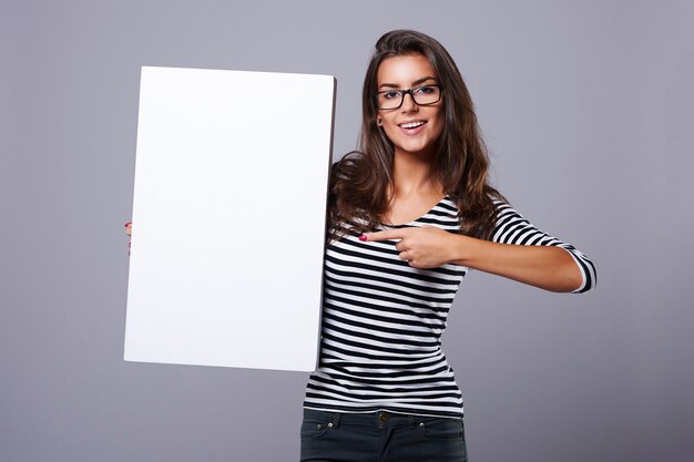 Prostokątny biały plakat trzymany przez atrakcyjną brunetkę