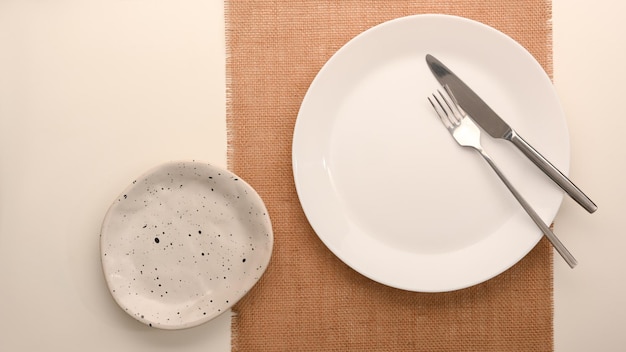 Prosty, minimalistyczny biały talerz ze sztućcami na podkładce na stole. widok z góry
