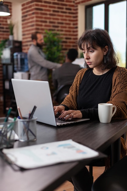 Przedsiębiorca kobieta analizuje statystyki firmy wpisując strategię marketingową na laptopie pracującym w biurze startowym. Menedżer wykonawczy przeprowadzający burze mózgów, dotyczące planowania współpracy biznesowej