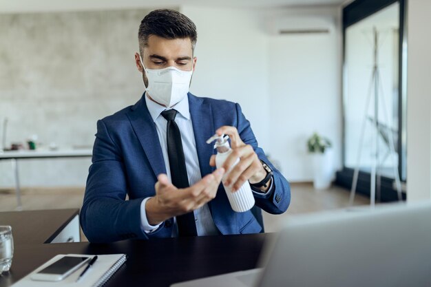 Przedsiębiorca z maską ochronną na twarz używający środka dezynfekującego do rąk w gabinecie
