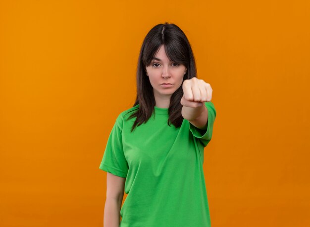 Przekonana, młoda dziewczyna kaukaski w zielonej koszuli pokazuje gest ręki pięści na na białym tle pomarańczowym tle z miejsca na kopię