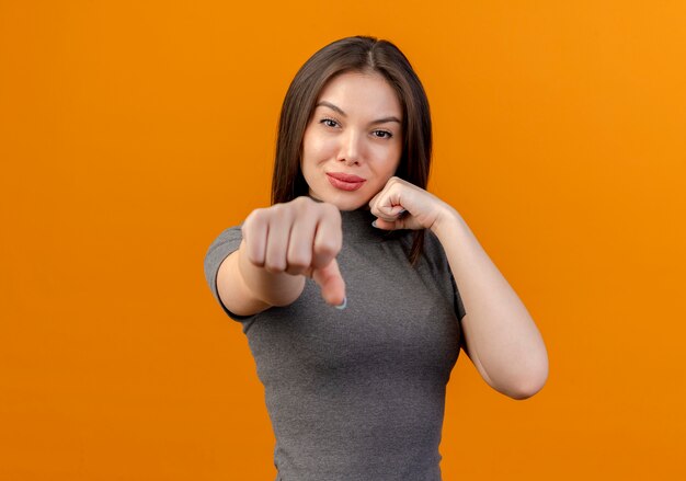 Przekonana, młoda ładna kobieta robi gest boksu w aparacie na białym tle na pomarańczowym tle z miejsca na kopię