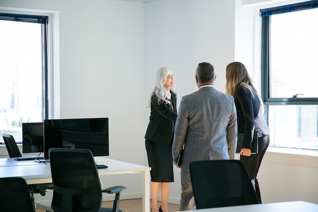 Bezpłatne zdjęcie przekonana, siwowłosa bizneswoman pozdrowienia kolegów w biurze. profesjonalny uścisk dłoni menadżera, uśmiechanie się i spotkanie w celu wspólnej dyskusji nad projektem. koncepcja biznesu i komunikacji