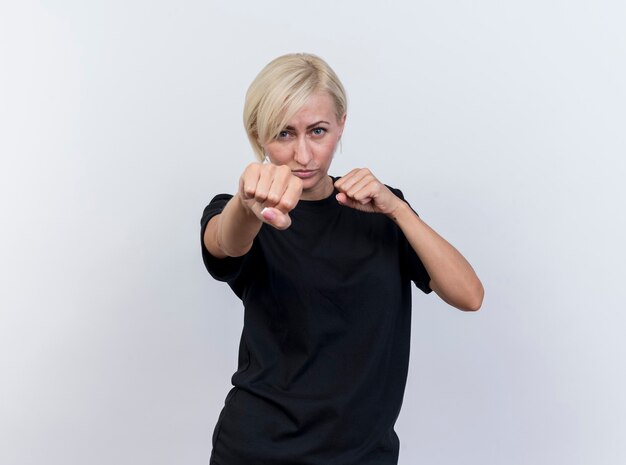 Przekonana w średnim wieku blond słowiańska kobieta, patrząc na kamery, robi gest boksu na białym tle na białym tle z miejsca na kopię