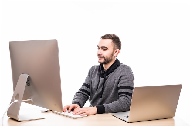 Przekonany, młody przedsiębiorca siedzi przy stole z laptopem i komputerem na białym tle