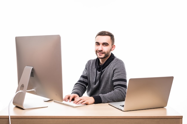 Przekonany, młody przedsiębiorca siedzi przy stole z laptopem i komputerem, patrząc na kamery na białym tle