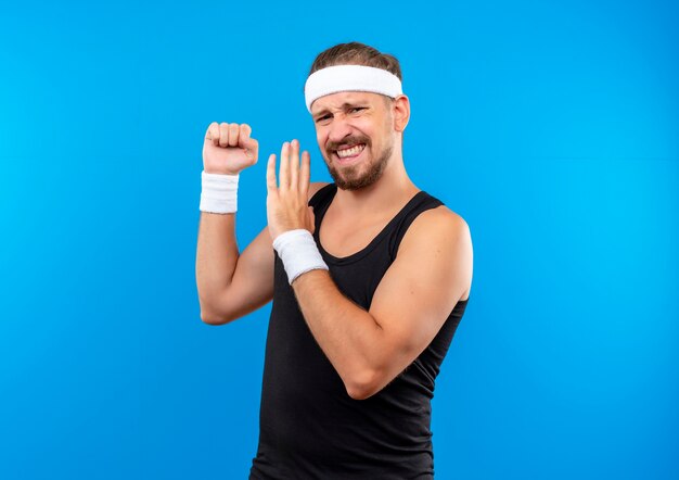 Przekonany, młody przystojny sportowy mężczyzna nosi opaskę i opaski, zaciskając pięść i wskazując ręką na to na białym tle na niebieskiej ścianie z kopią przestrzeni