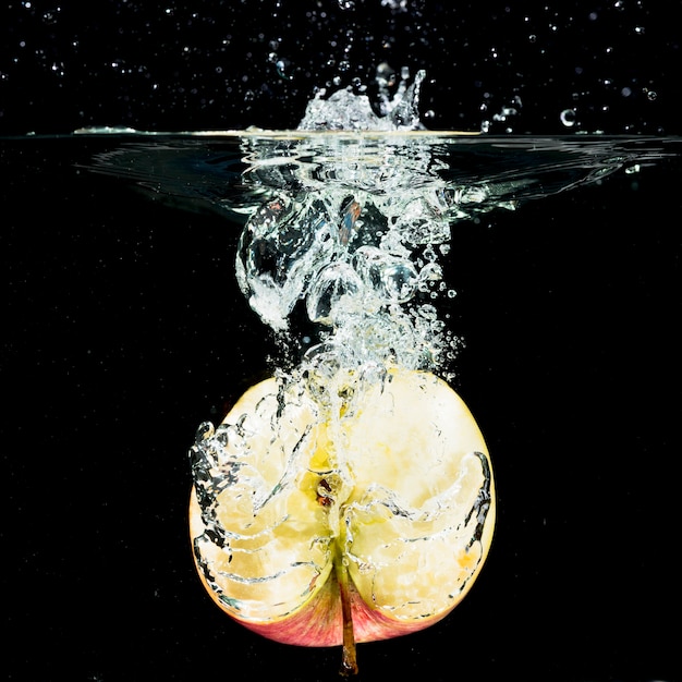 Przekrawający świeży jabłko spada w czystą wodę przeciw czarnemu tłu
