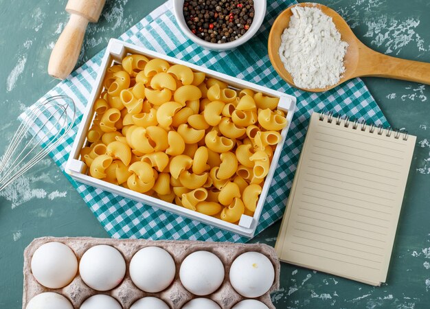 Przełóż makaron rigate w pudełku z jajkami, pieprzem, skrobią, wałkiem do ciasta, trzepaczką i zeszytem
