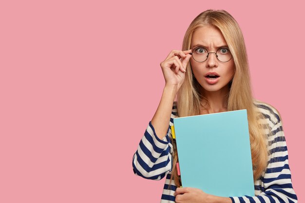 przerażona blond studentka pozuje na różowej ścianie
