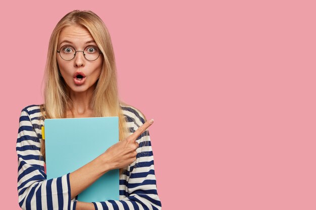 Przerażona blond studentka pozuje przy różowej ścianie