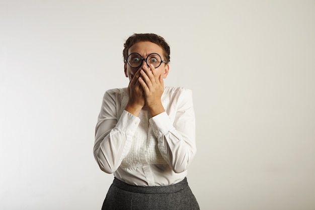 Bezpłatne zdjęcie przestraszona nauczycielka w białej bluzce i szarej spódniczce zakrywa usta rękami i krzyczy