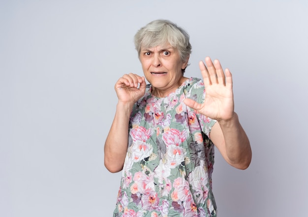 Przestraszona starsza kobieta stoi z uniesionymi rękami na białym tle na białej ścianie