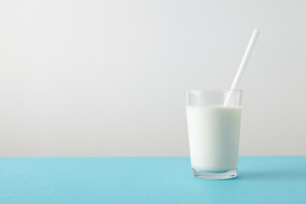 Przezroczyste szkło ze świeżym organicznym mlekiem i białą słomką wewnątrz na białym tle na pastelowym niebieskim stole