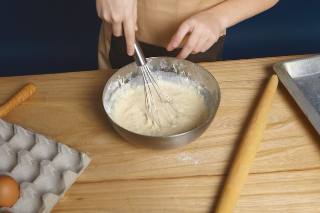 Przycięte ujęcie rąk trzymających trzepak podczas ubijania jajek mąką na ciastka sosnowe w metalowej misce.