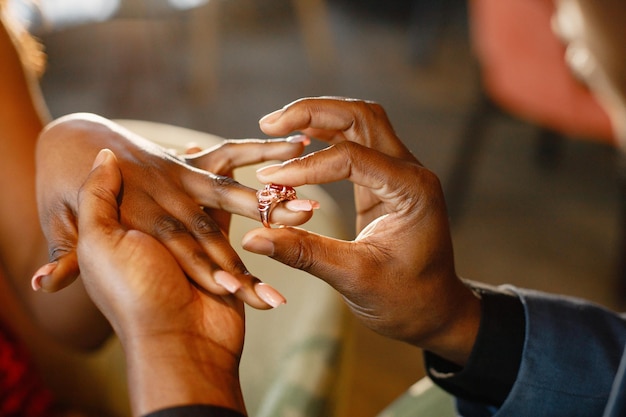 Przycięte zdjęcie dłoni czarnego mężczyzny noszącego pierścionek zaręczynowy na palcu swojej dziewczyny