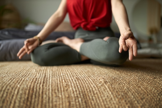Przycięty portret bosej kobiety w leginsach siedzącej na dywanie w pozycji lotosu ćwiczącej medytację w celu zmniejszenia stresu