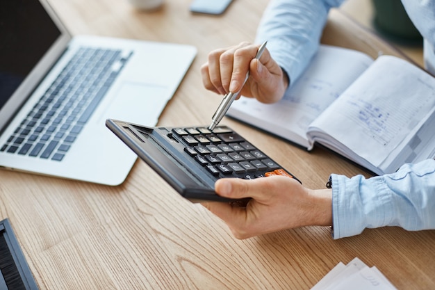 Bezpłatne zdjęcie przycięty widok profesjonalnego poważnego menedżera finansów, trzymając w rękach kalkulator, sprawdzając zyski z miesiąca firmy
