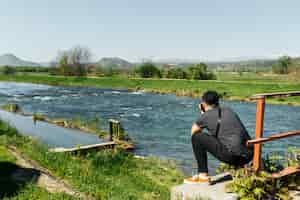Bezpłatne zdjęcie przyczajony mężczyzna biorąc zdjęcie idyllicznej rzeki