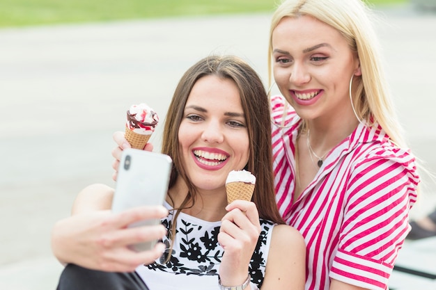 Bezpłatne zdjęcie przyjaciele bierze selfie podczas gdy jedzący lody rożek z telefonem komórkowym