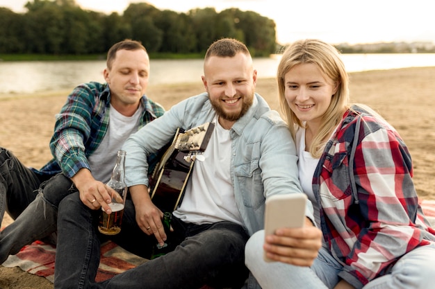 Przyjaciele biorąc selfie siedząc na piasku