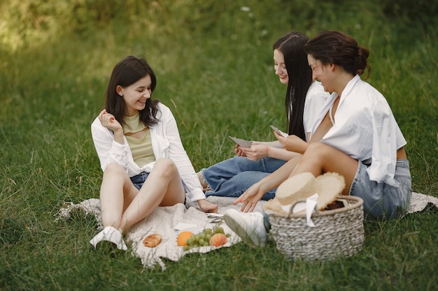 Przyjaciele siedzą na trawie. Dziewczyny na kocu. Kobieta w białej koszuli.