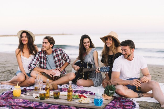 Przyjaciele siedzi na plaży z gitarą