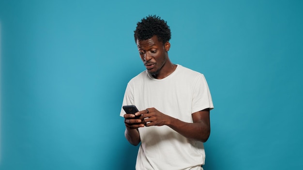 Przypadkowa osoba patrząc na smartfona i taniec w studio. Radosny mężczyzna słucha muzyki i piosenki, trzymając telefon z ekranem dotykowym w ręku, stojąc na na białym tle.