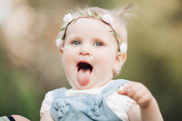 Przystojna dziewczynka z krótkie jasne włosy i ładny uśmiech w białej sukni siedzi na trawie w parku latem i uśmiecha się