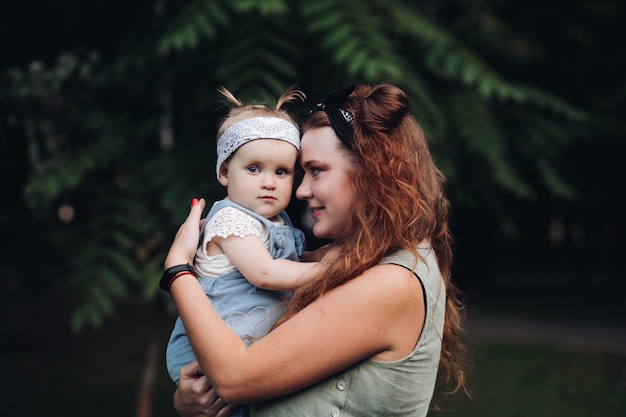 Przystojna Dziewczynka Z Krótkimi Jasnymi Włosami I ładnym Uśmiechem W Białej Sukience Siedzi Na Trawie W Parku Latem Z Matką