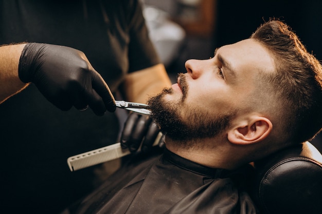 Przystojnego mężczyzna tnąca broda przy fryzjera męskiego sklepu salonem