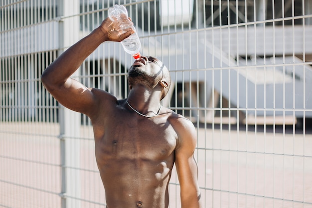 Przystojny African American człowiek z naga skrzynia pozuje z butelką wody