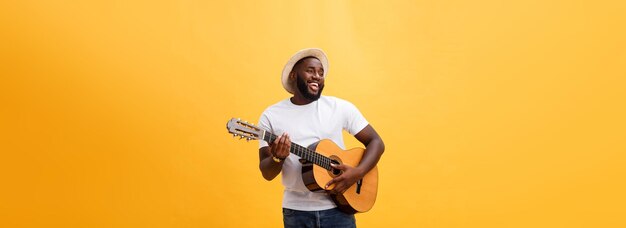 Przystojny afroamerykański gitarzysta w stylu retro grający na gitarze akustycznej na żółtym tle