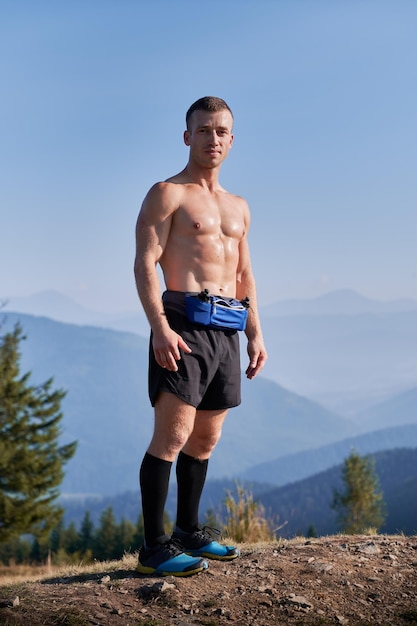Przystojny biegacz sportowy stojący na szczycie górskiego wzgórza