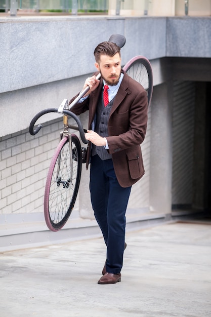 Przystojny biznesmen niosąc swój rower na ulicach miasta. Pojęcie nowoczesnego stylu życia młodych mężczyzn