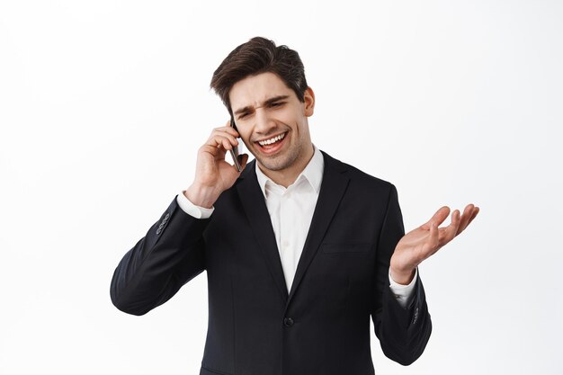 Przystojny biznesmen prowadzący rozmowę biznesową na telefonie komórkowym, uśmiechający się i mówiący „tak”, wyrażający zgodę, wyglądający na usatysfakcjonowanego podczas rozmowy, białe tło