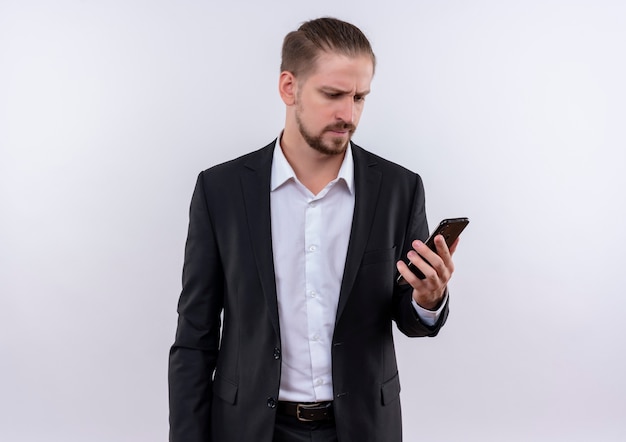 Przystojny biznesmen ubrany w garnitur, patrząc na swojego smartfona zdezorientowany stojąc na białym tle