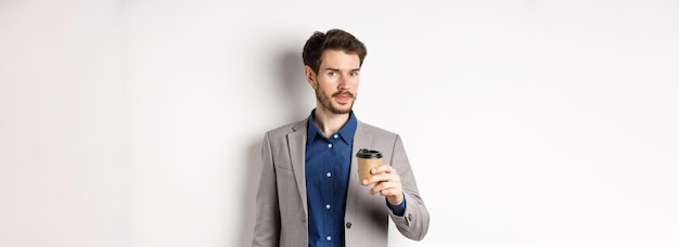 Przystojny biznesmen w garniturze pijący kawę i patrzący na kamerę stojącą na białym tle