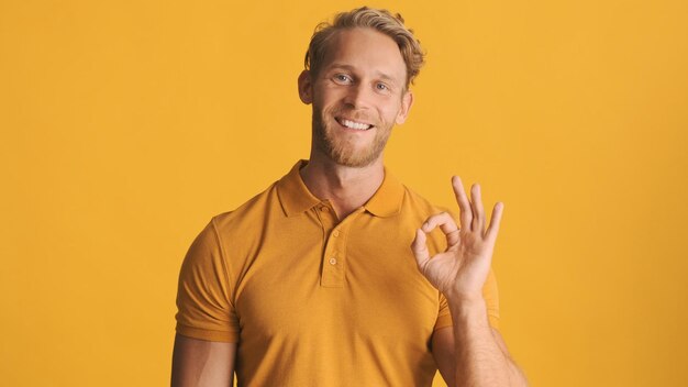 Przystojny blond brodaty mężczyzna pokazujący ok gest zgadzający się z przyjacielem w aparacie na kolorowym tle Dobra robota wyrażenie