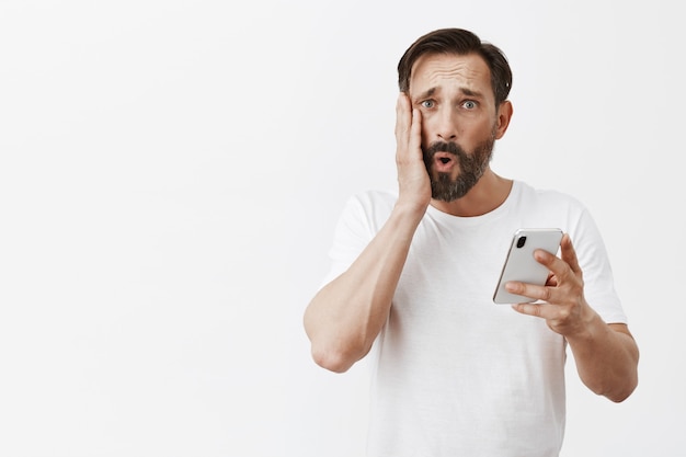 Przystojny brodaty dojrzały mężczyzna pozuje z jego telefonem