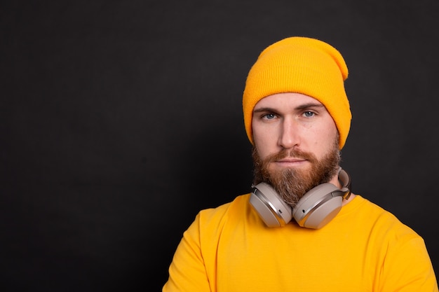 Przystojny Brodaty mężczyzna hipster żółty kapelusz t shirt ze słuchawkami na białym tle na czarnym tle