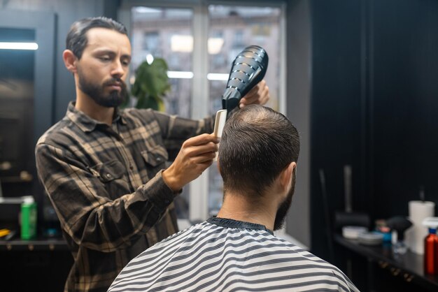 Przystojny brodaty mężczyzna robi fryzurę przez fryzjera w zakładzie fryzjerskim